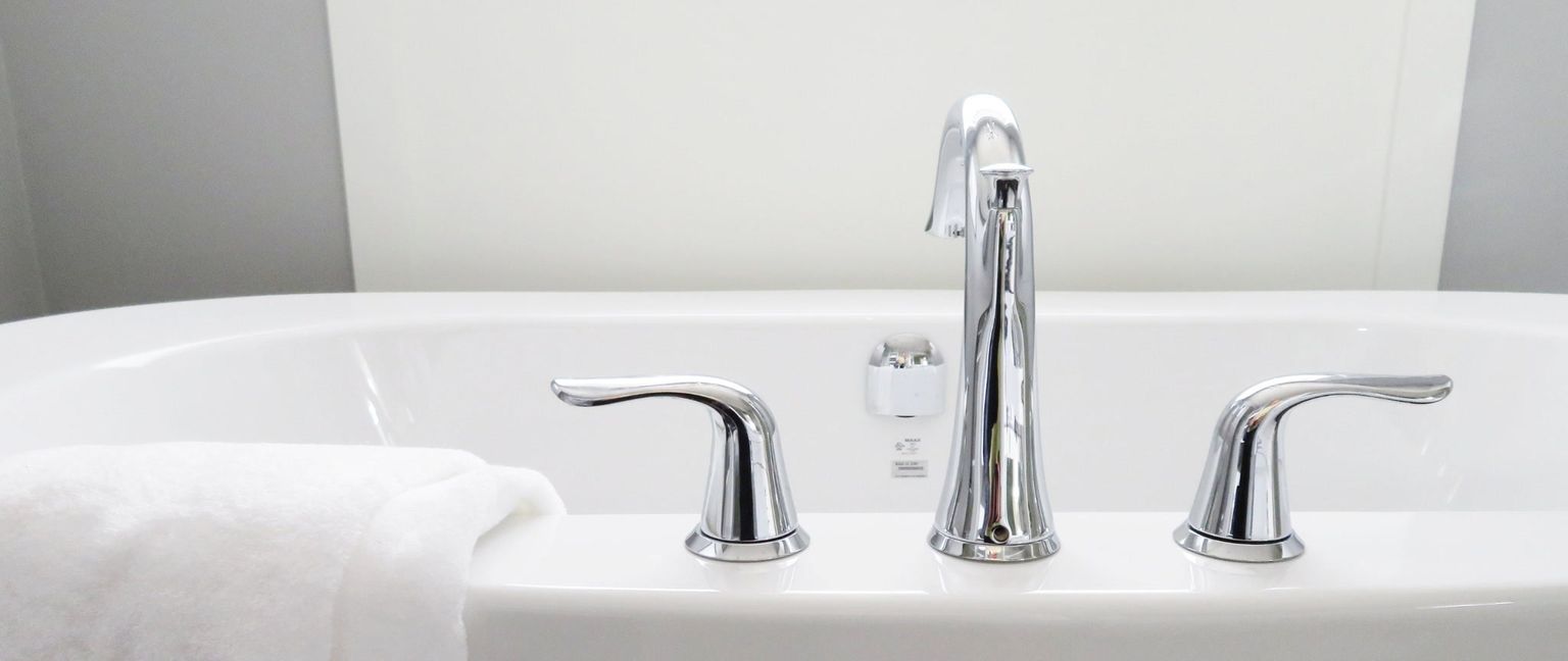 Close-up of a chrome bathtub faucet and handles with a white towel draped over the edge of the tub.
