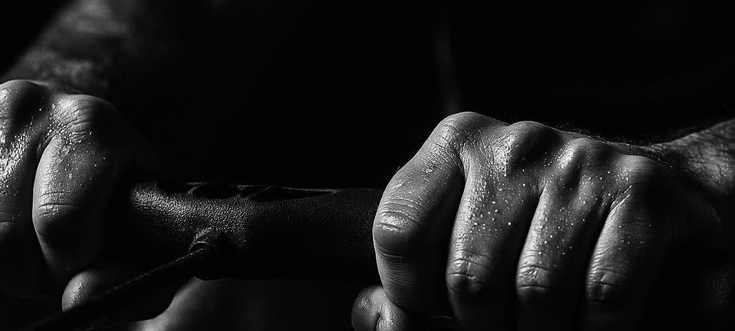 Close-up of hands tightly gripping the handle of a rowing machine, showing the intensity of the workout.