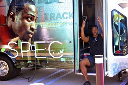 James Anderson, a professional athlete, is sitting in the doorway of a bus with a large graphic of his face on the side of the bus.