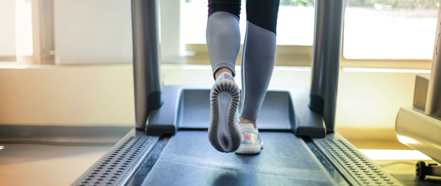 A person's legs and feet, wearing athletic shoes and leggings, as they walk on a treadmill.