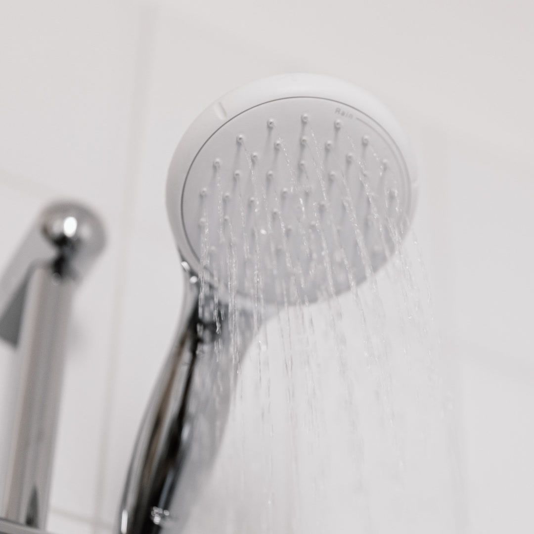 Close-up of a white shower head spraying water against a tiled wall.