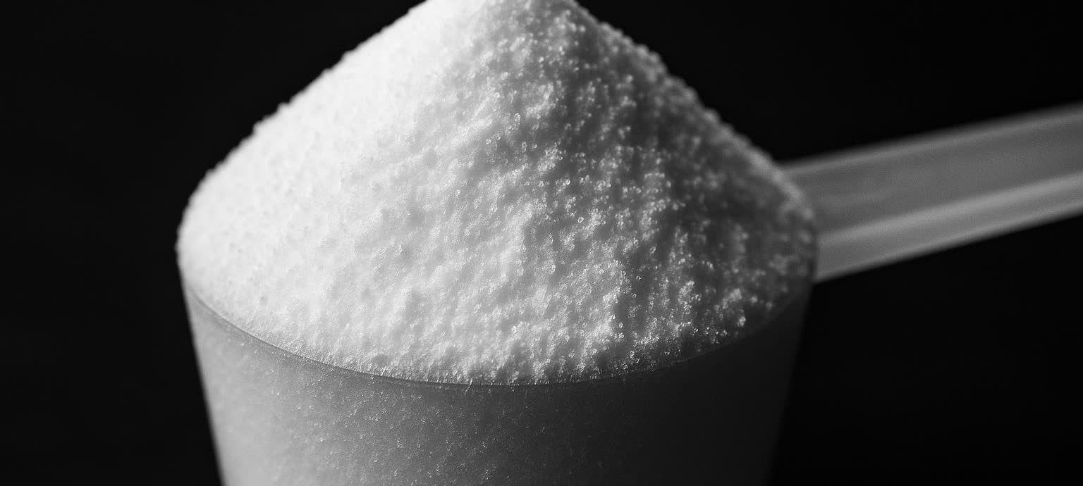 A close-up macro shot of a scoop filled with pure white creatine monohydrate powder against a dark black background.