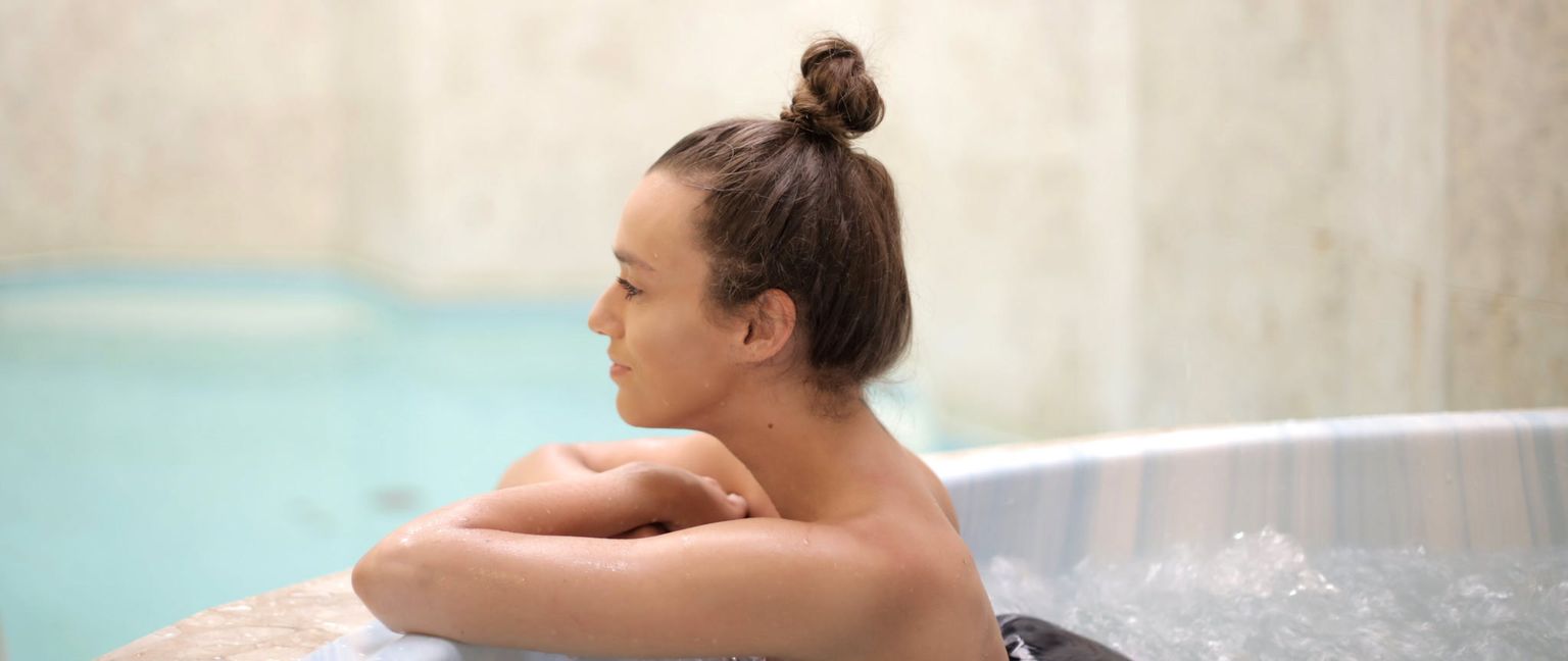 A woman leans on the edge of a bubbling ice bath with her arms crossed, looking off to the side.