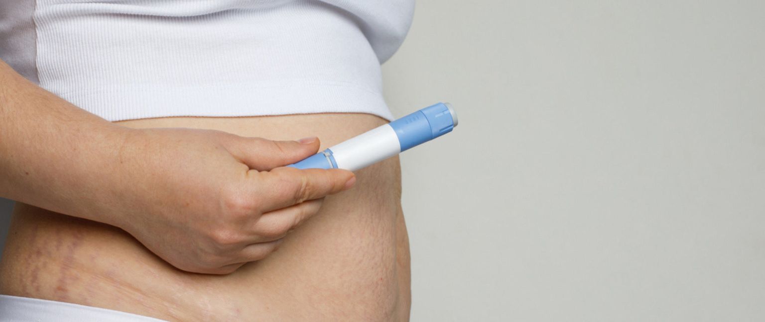 Woman holding Ozempic pens near her stomach, preparing for an injection.