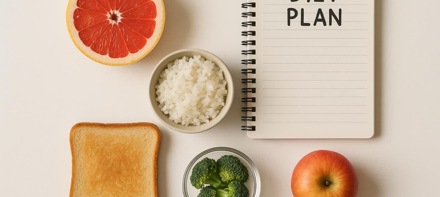 Top-down view of precisely arranged diet food including a grapefruit half, a slice of toast, a bowl of white rice, a bowl of broccoli florets, and an apple. A spiral notebook open to a page with 'DIET PLAN' written at the top is also visible, symbolizing a strict meal plan.