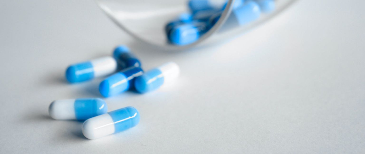 Several blue and white capsules are spilled on a white surface next to a partially visible container.