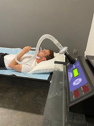 A man lies on a bed with a mask over his mouth and nose connected to a tube for a resting metabolic rate (RMR) test.
