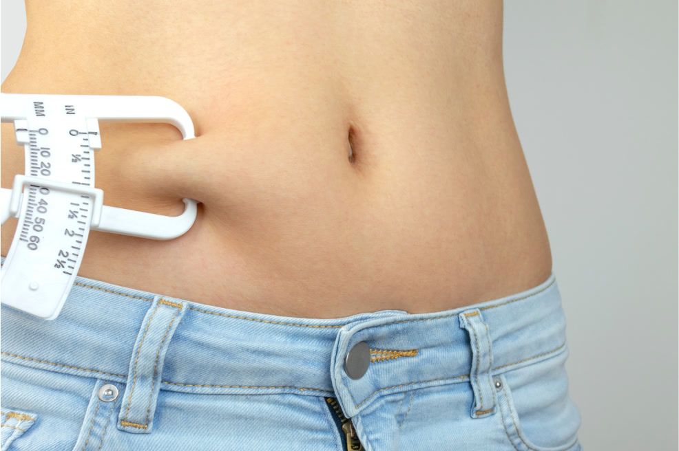 Close-up of a person's stomach being measured for subcutaneous fat using a caliper.