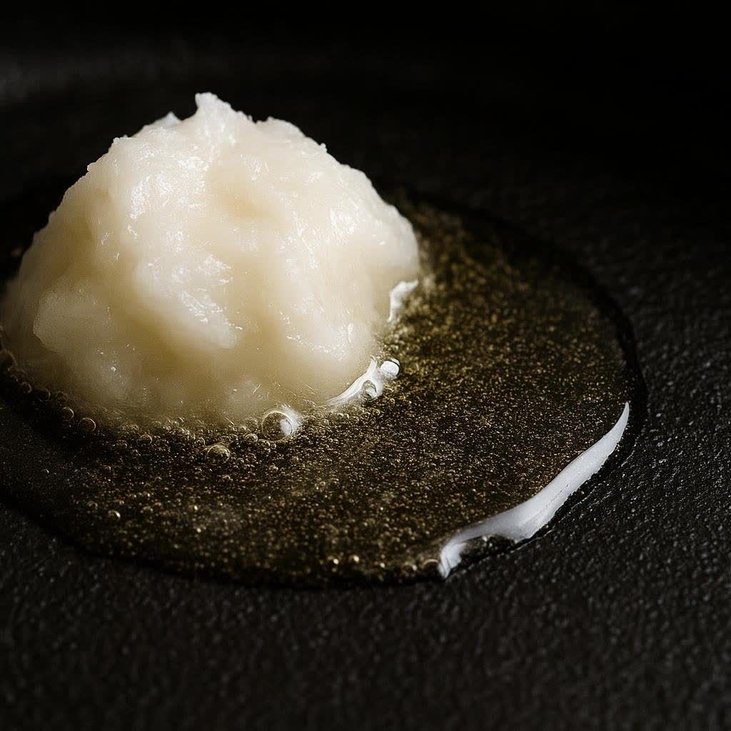 A close-up shot of white beef tallow melting into a clear, golden liquid in a dark, hot pan, with small bubbles forming.