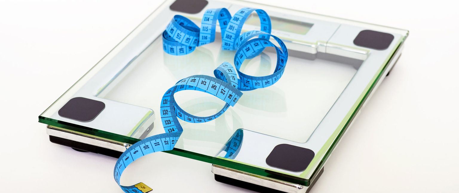 A weight scale with a blue measuring tape draped across it.