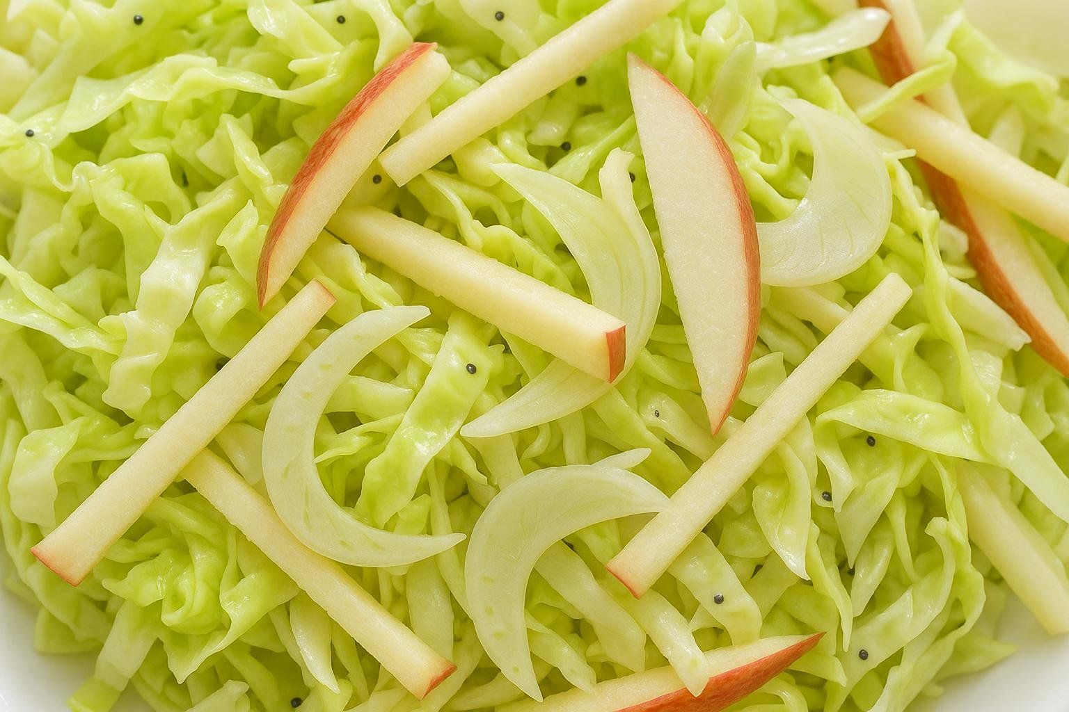 A close-up shot of a crunchy apple-fennel slaw, showing the texture of shredded cabbage and apple sticks.
