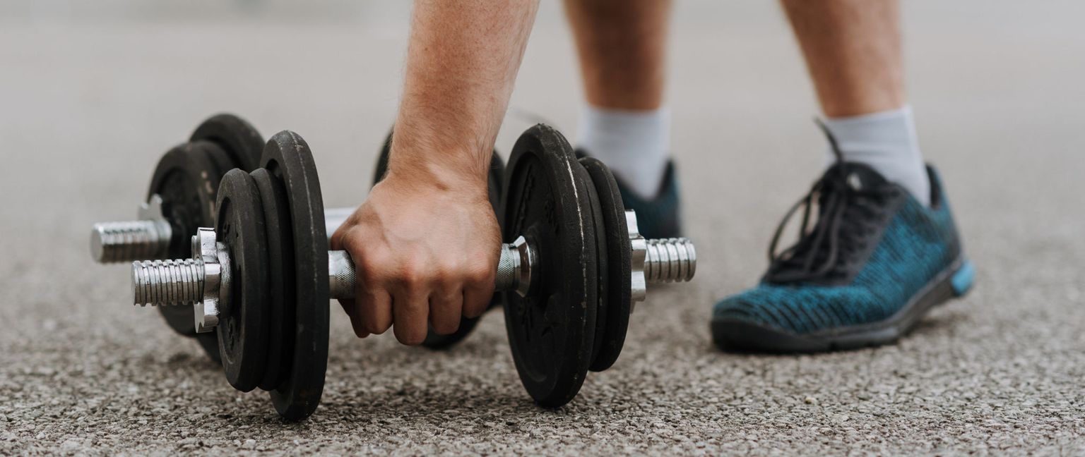 Close up of a person reaching down to pick up a dumbbell. Their blue and black sneakers are visible in the background.