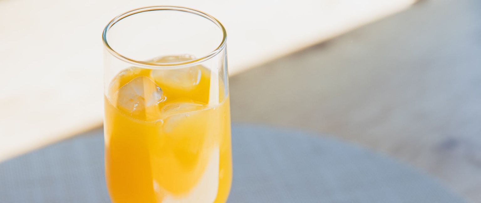 A close-up, top-down view of a glass filled with bright orange juice and ice cubes.