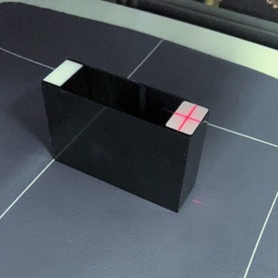 A black rectangular block with white markers on each end. A red laser beam is visible, forming a cross on one of the white markers.