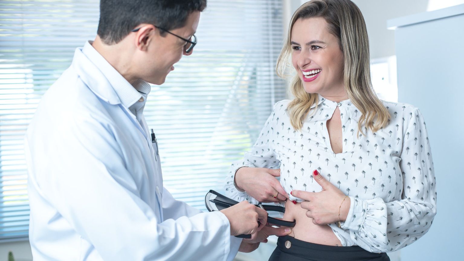 A doctor using calipers to measure the body fat of a smiling woman.