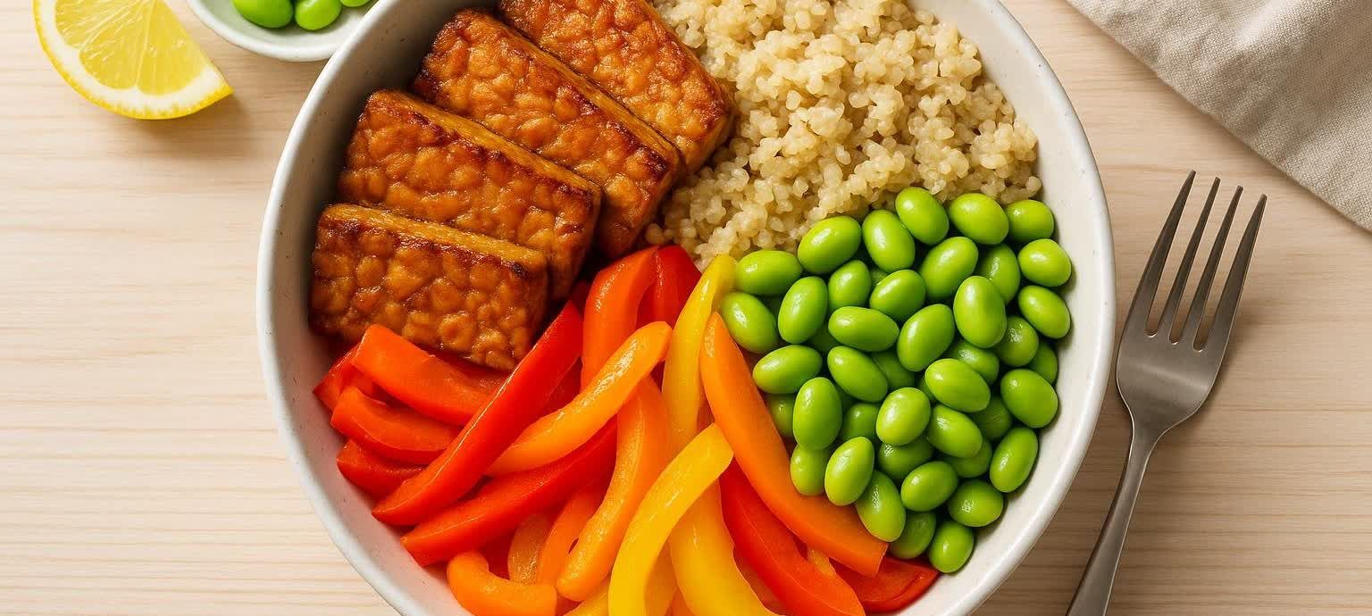 A top-down view of a colorful and appetizing high-protein vegan power bowl with tempeh and quinoa on a light wooden surface.