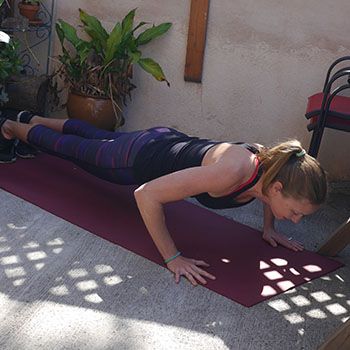 A woman in workout clothes is doing a pushup on a purple yoga mat outdoors.