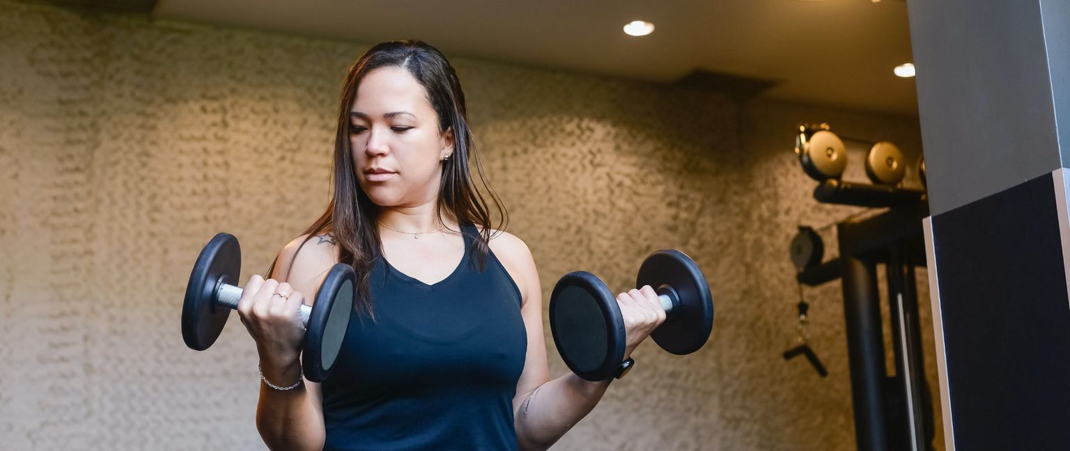 A woman performs bicep curls with dumbbells in a gym.