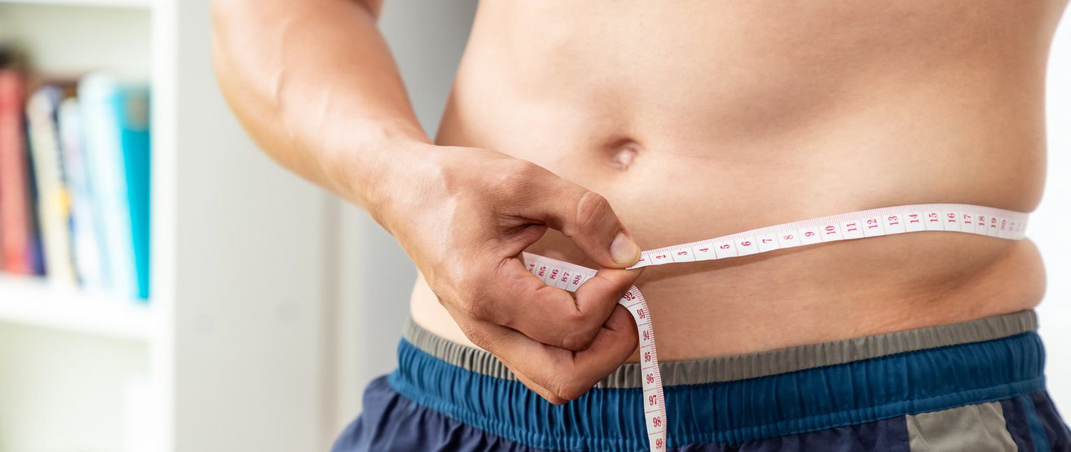 A close-up shot of a man measuring his waist with a white measuring tape.