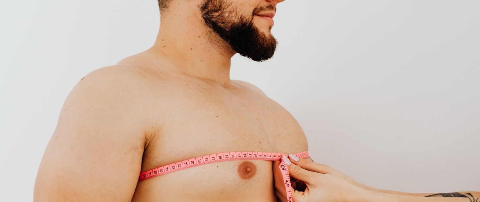 A man has his chest measured with a pink measuring tape.