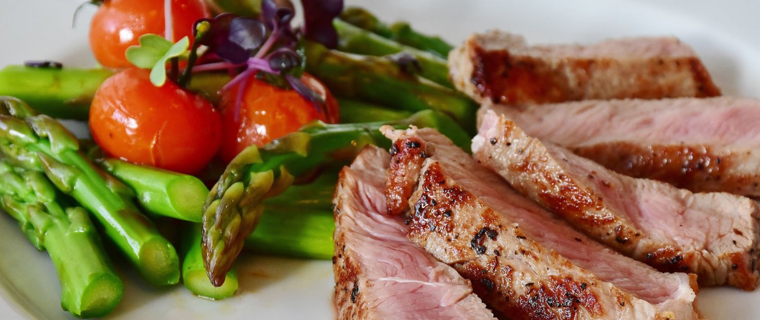 Close up of sliced steak with asparagus and cherry tomatoes.