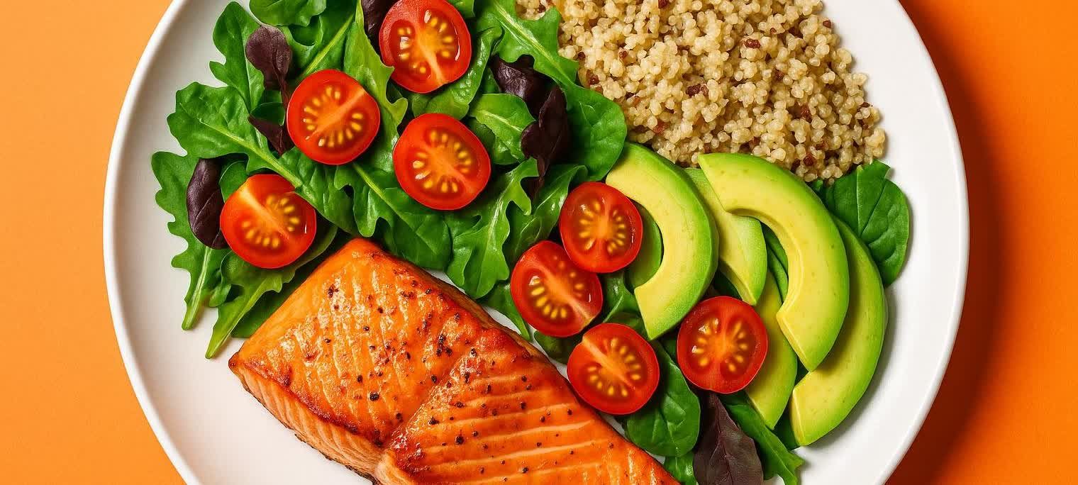 A top-down view of a healthy and balanced meal served on a white plate. The meal features a cooked salmon fillet, fresh green salad with rocket and cherry tomatoes, sliced avocado, and a side of quinoa. The plate is set against a vibrant orange background.