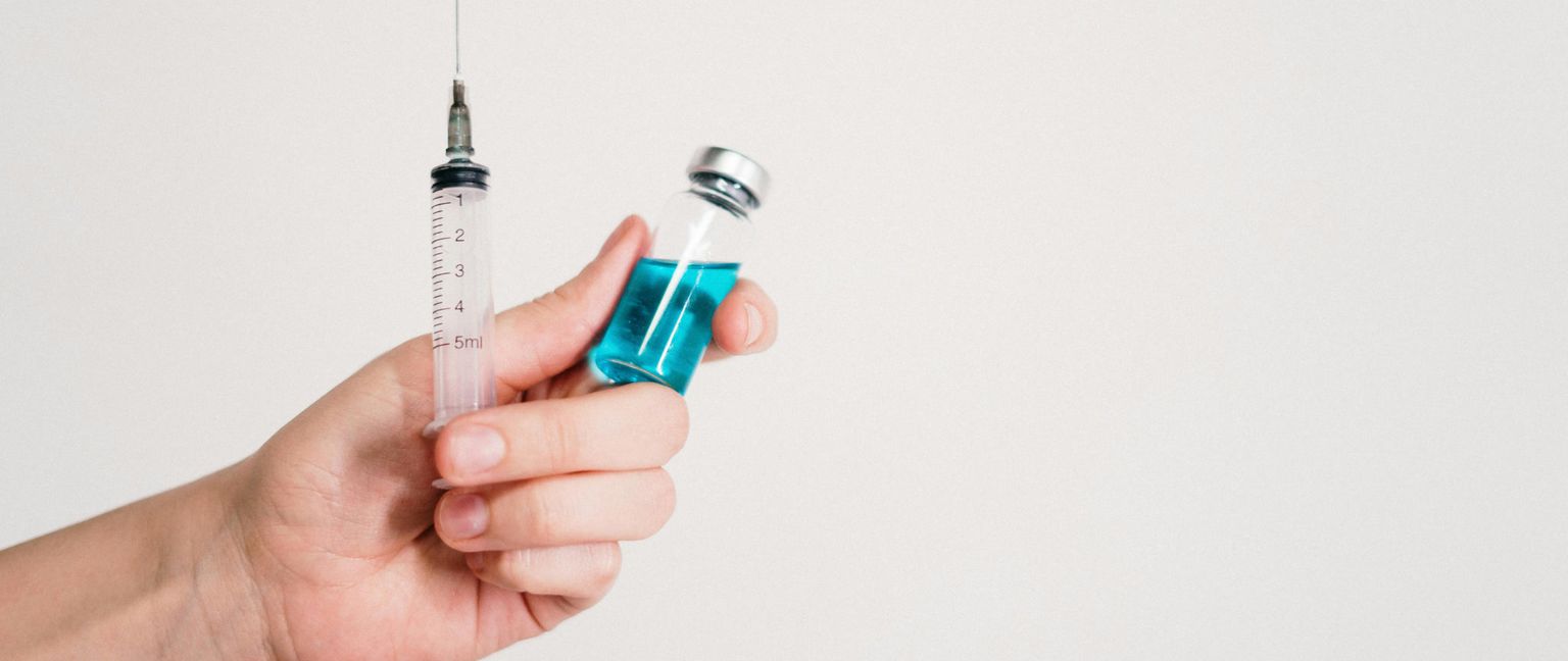 A hand holds a syringe next to a small bottle containing blue liquid.