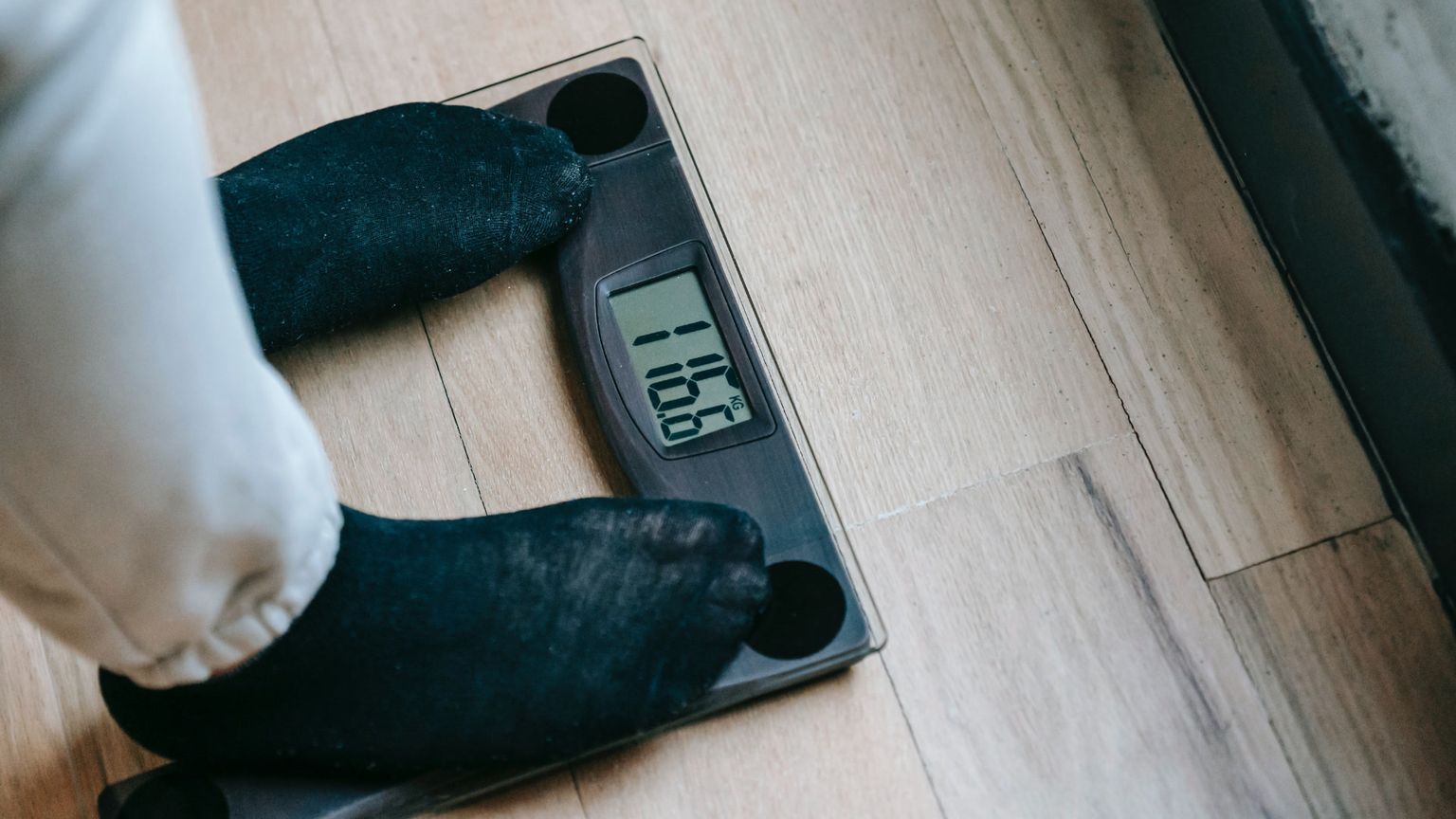 Closeup of a person's feet in dark socks standing on a digital scale displaying a weight.