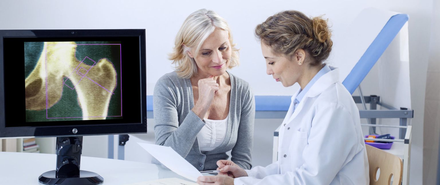 A doctor and a middle-aged woman are looking at a bone density scan of a hip on a computer monitor.