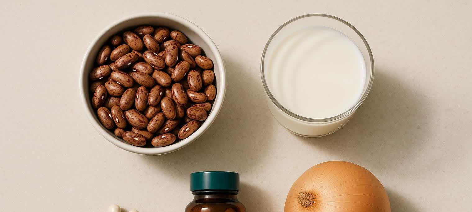 A top-down view of a bowl of pinto beans, a glass of milk, an onion, and a bottle of digestive enzymes with pills scattered nearby. These items represent common trigger foods and a solution.