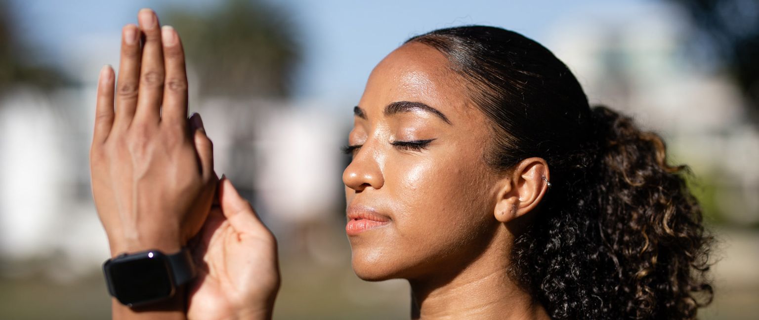 A woman with a fitness tracker on her wrist stretches with her eyes closed and a peaceful expression.